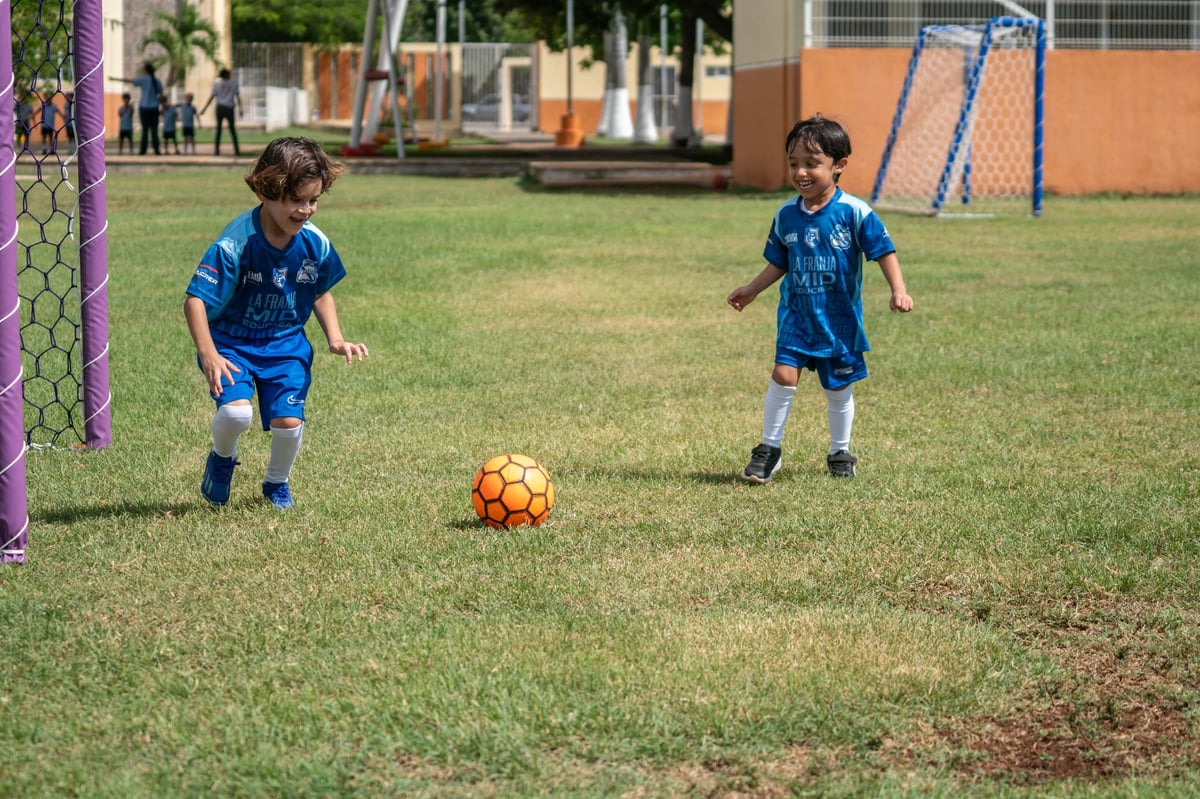 Dos niños con camisetas azules jugando fútbol en un campo de pasto durante el entrenamiento